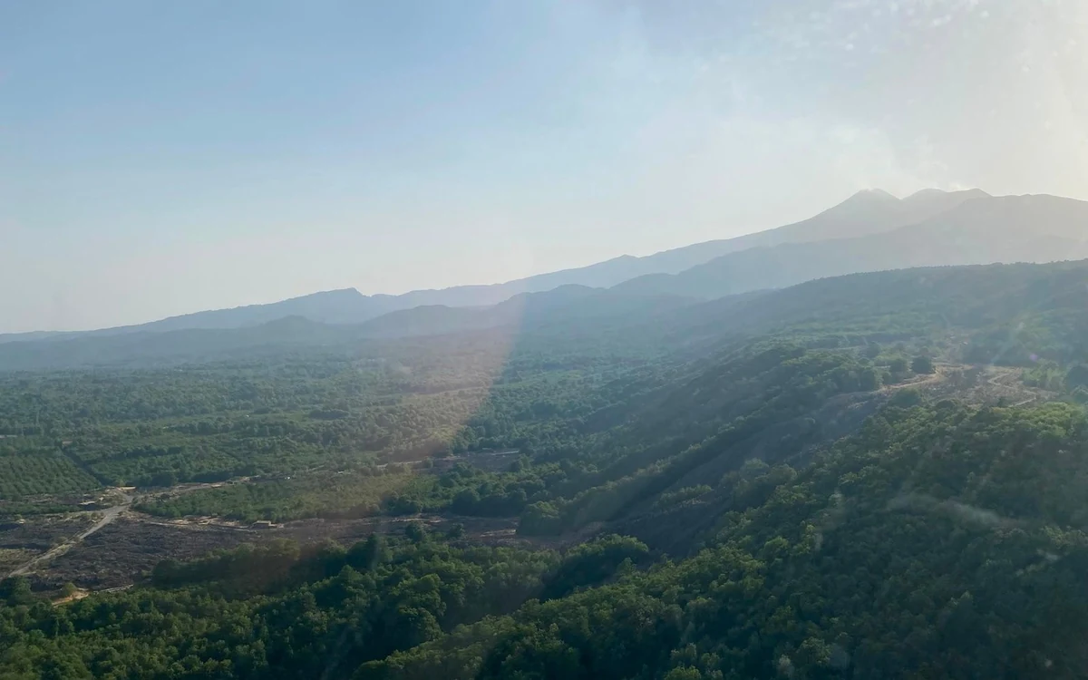 A helicopter flying along the Ionian coast of Sicily with the sea on one side and the slopes of Etna rising inland