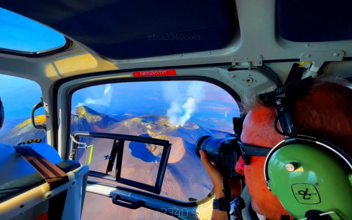 Passengers seated in the cabin of a helicopter with headsets on, looking out of the side window towards Etna