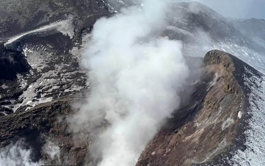 A helicopter over the wooded lower slopes of Mount Etna with the coast behind it