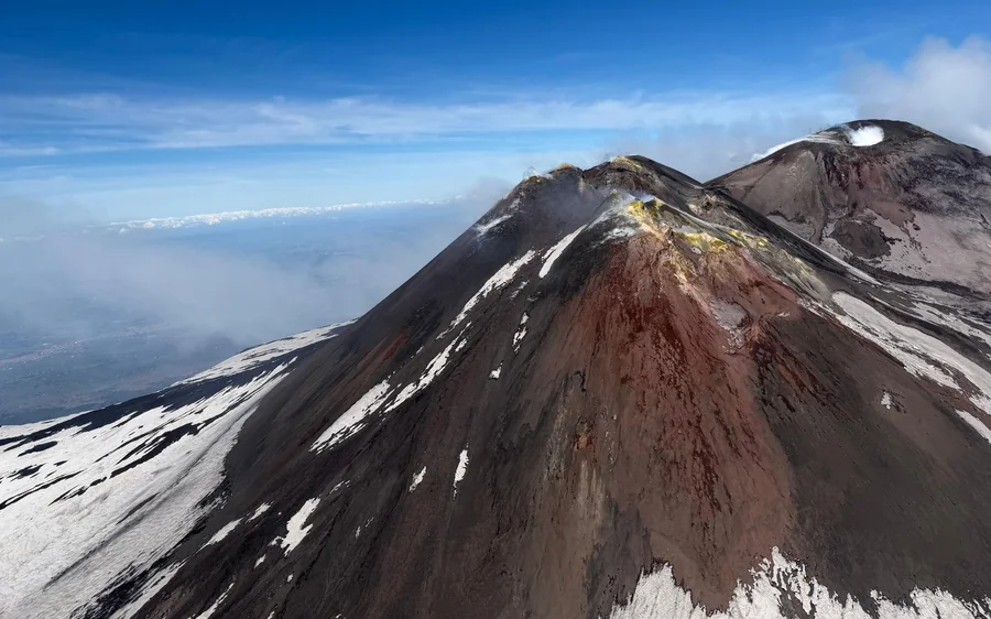 Passengers in the cabin of a small helicopter looking out over a volcanic slope