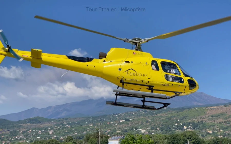 A helicopter on the ground high on Mount Etna with the crater rim beyond it
